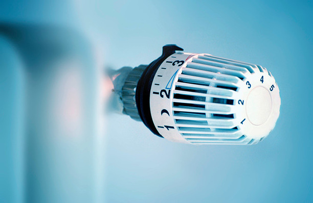 Nahaufnahme eines weißen Heizkörperthermostats mit nummerierten Wählscheibeneinstellungen vor einem blauen Hintergrund. - © Bild: emmi - stock.adobe.com