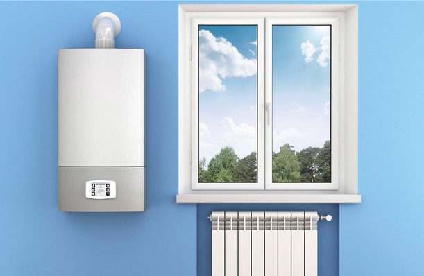 An der Wand montierter Heizkessel und Heizkörper unter einem Fenster mit Blick auf Bäume und Himmel vor einer blauen Wand. - © Bild: Getty Images/iStockphoto