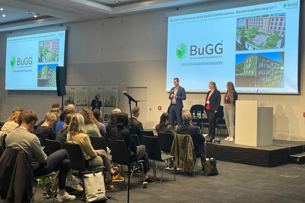© Alisia Romeo BuGG-Präsident Gunter Mann begrüßt die Teilnehmenden auf der Bühne mit Sylvia van Meegen, Assistentin und Michelle Bruchmüller, Veranstaltungsmanagerin (rechts außen).