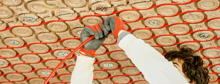 Person, die mit Handschuhen rote Drähte in ein Muster kreisförmiger Halterungen an der Decke einbaut. - © Bild: Lehmbau Schneider