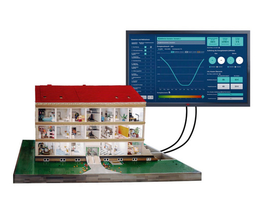 Modellhaus mit sichtbaren Innenräumen, die mit einem Monitor verkabelt sind, der Daten und Grafiken zum Energieverbrauch anzeigt. - © Bild: Stefan Thielicke
