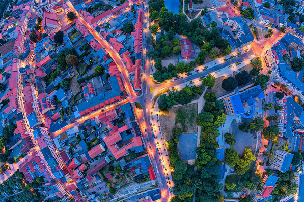 Luftaufnahme einer städtischen Kreuzung mit beleuchteten Straßen, Gebäuden und Grünflächen in der Abenddämmerung. - © Mathias Weil – stock.adobe.com